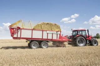 Červený traktor táhne samosběrací vůz Pöttinger Primo na poli