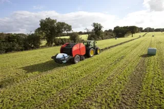 Traktor s lisem a baličkou kulatých balíků na louce