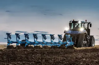 Modrý pásový traktor při orbě s modrým pluhem