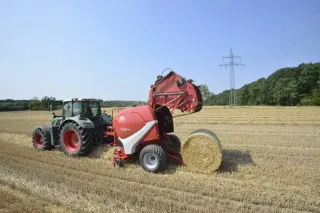 Traktor s červeným lisem Lely při lisování balíku