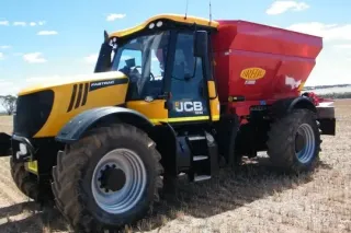 Žlutý traktor JCB se samojízdným rozmetadlem Bredal na poli.