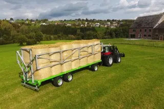 Traktor veze vůz Joskin Wago s balíky slámy.