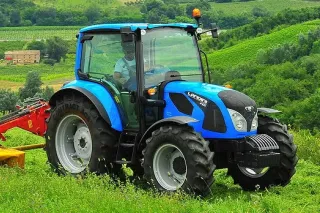 Modrý traktor Landini s připojeným nářadím na louce