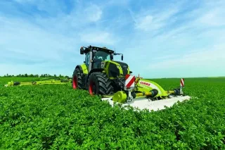 Zelený traktor Claas se žacím strojem na louce