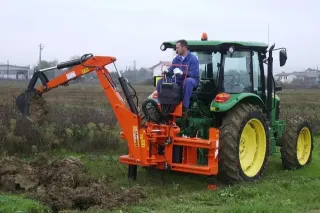 Oranžové rýpadlo Vogt namontované na zeleném traktoru při výkopových pracích.