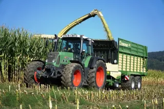 Zelený vůz Krone tažený traktorem při sklizni kukuřice