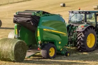 Zelený lis John Deere ukládá balík sena na poli