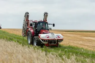 Červený traktor s postřikovačem u pole