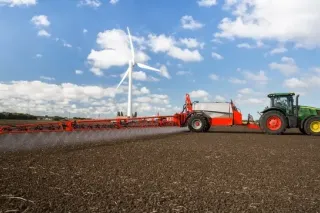 Traktor táhne červený postřikovač přes pole