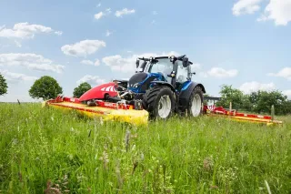 Modrý traktor s žacími stroji Fella na louce