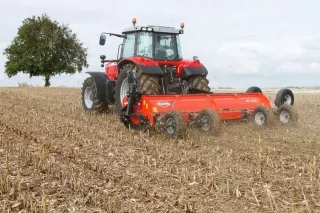 Červený traktor táhne stroj Kuhn po poli