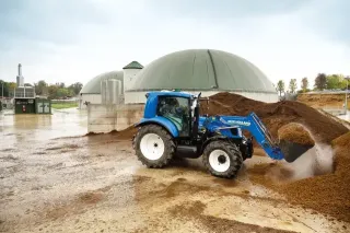 Modrý traktor New Holland nakládá materiál u bioplynové stanice