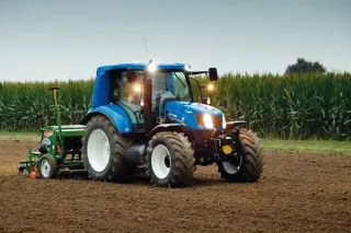 Modrý traktor New Holland se secím strojem na poli.