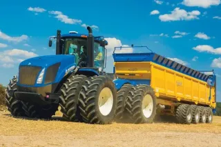 Modrý traktor New Holland táhne žlutý rozmetací návěs.