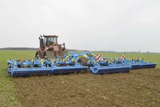 Široký modrý kypřič Bednar za traktorem na poli