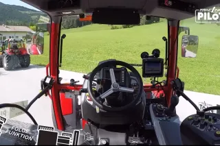 Pohled z kabiny traktoru na druhý traktor jedoucí po silnici.