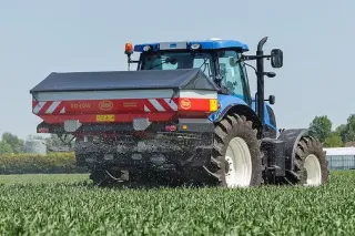 Modrý traktor s rozmetadlem Vicon při aplikaci hnojiva na poli