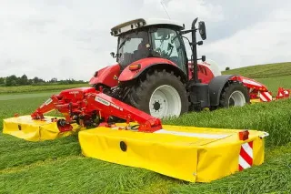 Červený traktor se žacím strojem Pöttinger Novacat na louce