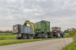Červený traktor s překládacím systémem Fliegl BÜFFEL při sklizni píce