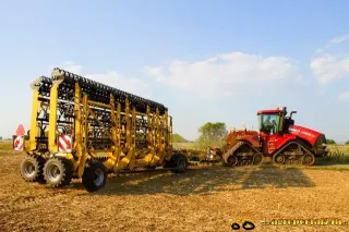 Červený pásový traktor Case IH Quadtrac se žlutým nářadím na poli