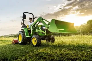 Kompaktní traktor John Deere s čelním nakladačem na louce