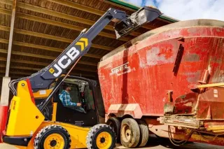 Žlutý smykem řízený nakladač JCB nakládající krmný vůz