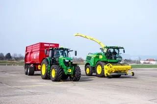 Zelený traktor s červeným vozem vedle řezačky na ploše