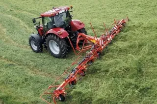 Červený traktor s širokým obracečem Kuhn při práci na louce