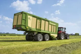 Zelený senážní vůz Krone tažený traktorem na louce