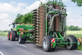 Traktor táhne složený zelený secí stroj Amazone po silnici