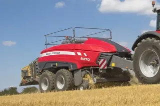 Červený lis Massey Ferguson tažený traktorem při lisování slámy
