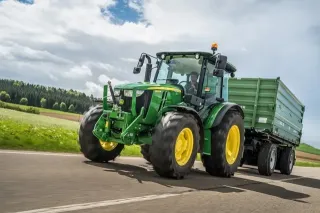 Zelený traktor John Deere táhne zemědělský přívěs po silnici