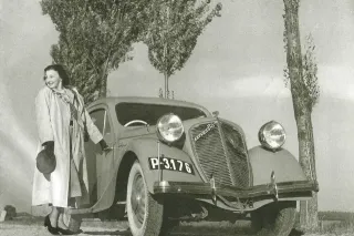 Historický automobil Zbrojovka Brno na černobílé fotografii s ženou u otevřených dveří.