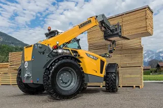 Žlutý teleskopický manipulátor Liebherr zvedá dřevěný náklad