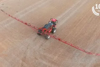 Traktor se širokým secím strojem na poli.