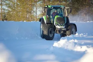 Zelený traktor Valtra projíždí sněhem