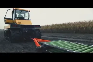 Starší žlutý zemědělský stroj při práci na poli s dopravníkem v popředí.