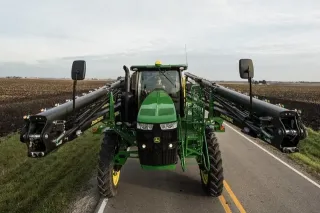 Zelený samojízdný postřikovač John Deere se složenými rameny na cestě.