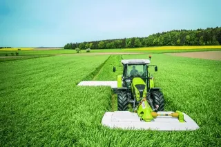 Zelený traktor Claas se žacími stroji na louce