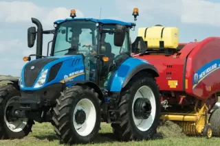Modrý traktor New Holland s červeným lisem na poli