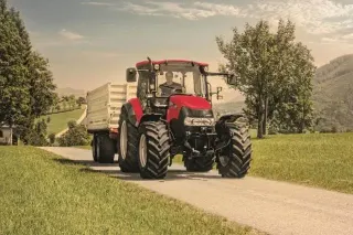 Červený traktor Case IH Farmall s přívěsem na cestě