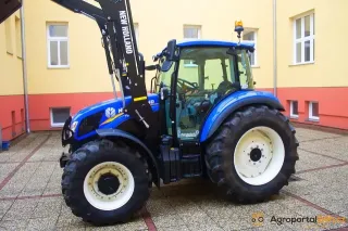Modrý traktor New Holland T5 s čelním nakladačem na dvoře školy