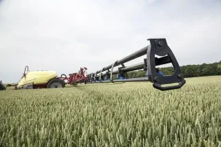Rameno taženého postřikovače nad obilným porostem