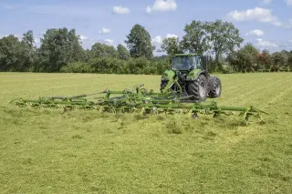 Traktor táhne široký zelený obraceč sena po louce