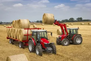Dva červené traktory Massey Ferguson při manipulaci s balíky