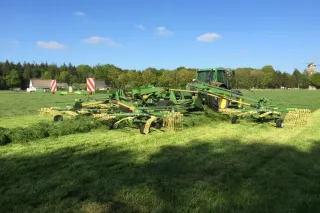 Traktor se širokým shrnovačem Krone na louce