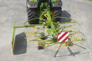 Zelený shrnovač píce připojený za traktorem