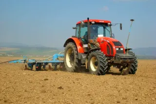 Červený traktor Zetor táhne modrý secí stroj po připraveném poli.