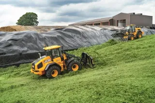 Dva žluté nakladače JCB při práci se siláží