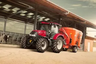 Červený traktor Case IH s krmným vozem u stáje